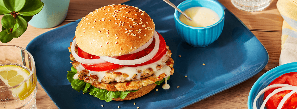 Chicken smashed burger on bun topped with Donair sauce, sliced tomato and onion.