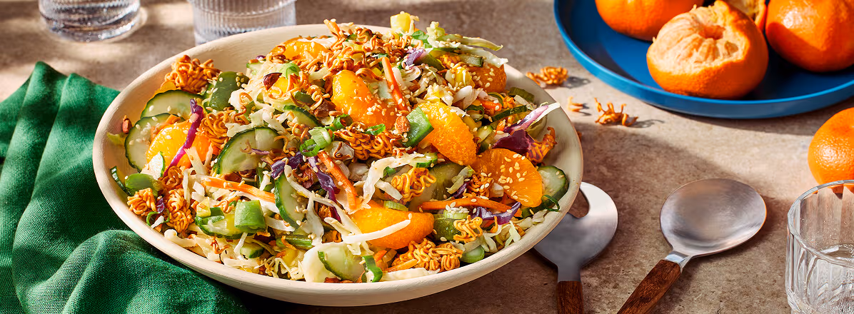 Asian ramen salad in a white bowl with mandarins in the background