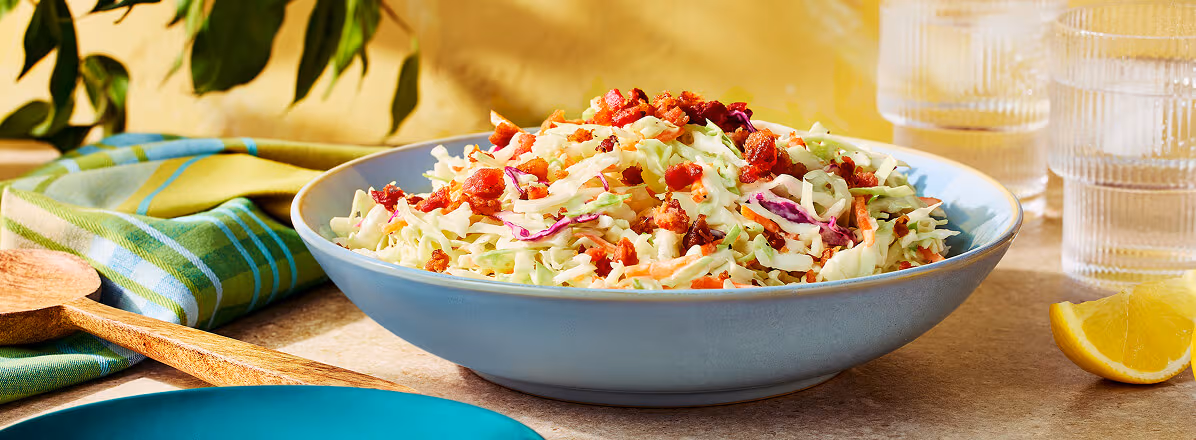 Caesar Salad Inspired Slaw in a white bowl topped with bacon bits