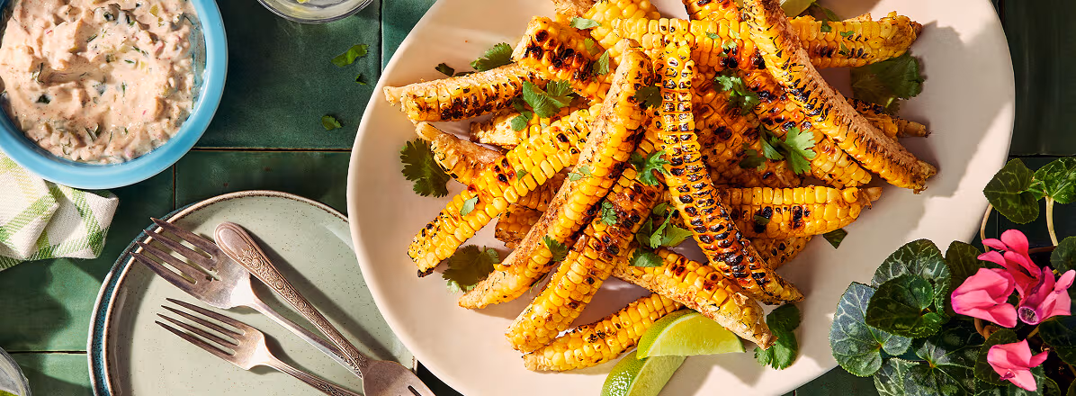 Overhead shot of corn ribs on a white plate, corn ribs have been charred and topped with spices, and cilantro