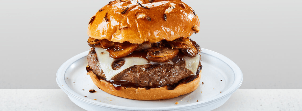 Shot of Mushroom Swiss Burger with pretzel bun topped with mushrooms and sliced Swiss cheese