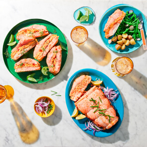 Mediterranean stuffed salmon on a green platter served with lime wedges next to a glass of water on a white marble tabletop.