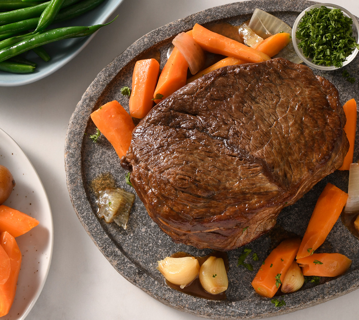 Boneless cross rib pot roast on black plate with roasted carrots