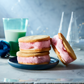 Pink cotton candy sandwiched between two sugar cookies on a blue plate  next to a glass of milk