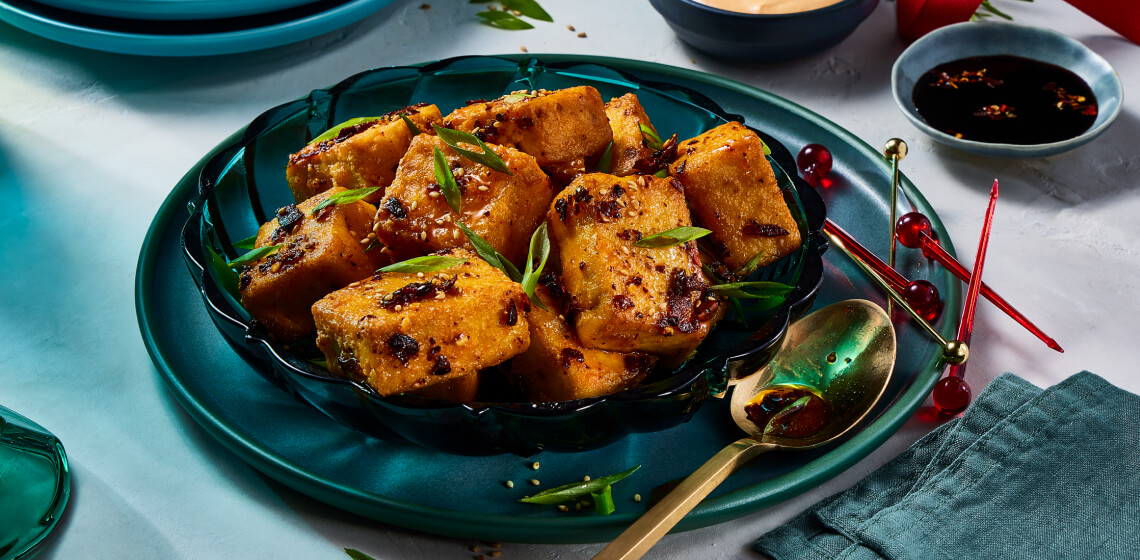 Chili crisp tofu bites on top of blue plate with sauces on the side