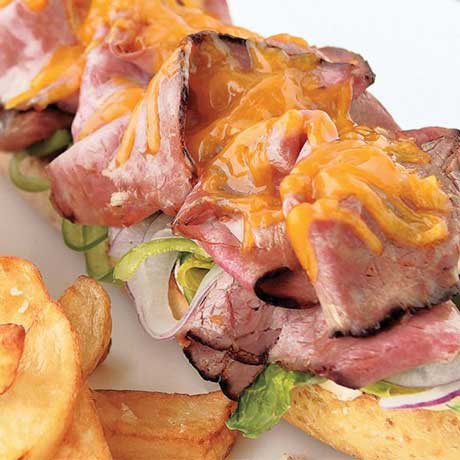 Roast beef sandwich with melted cheese and chipotle served next to oven-baked fries and a small ramekin of coleslaw on a white plate.