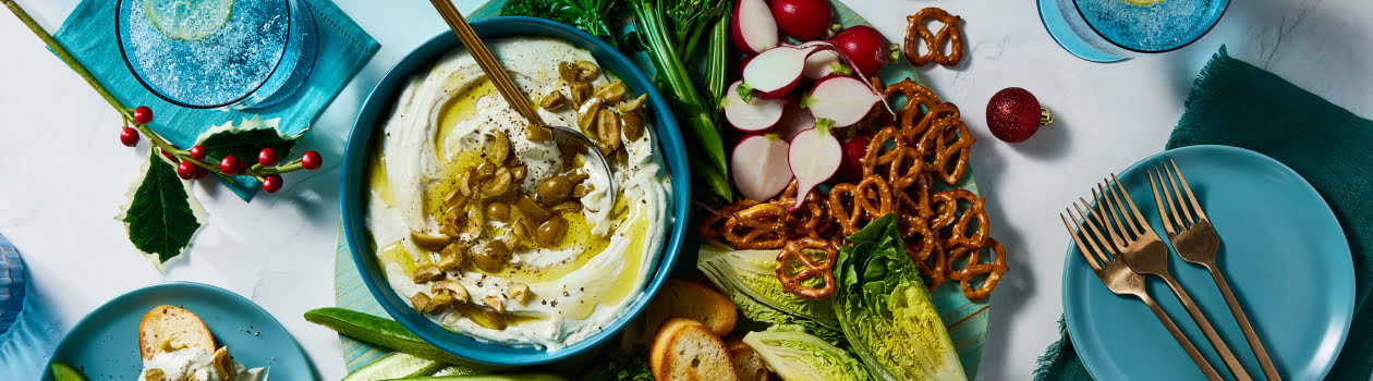 Overhead shot of dirty martini dip with baguette, vegetables, and pretzels