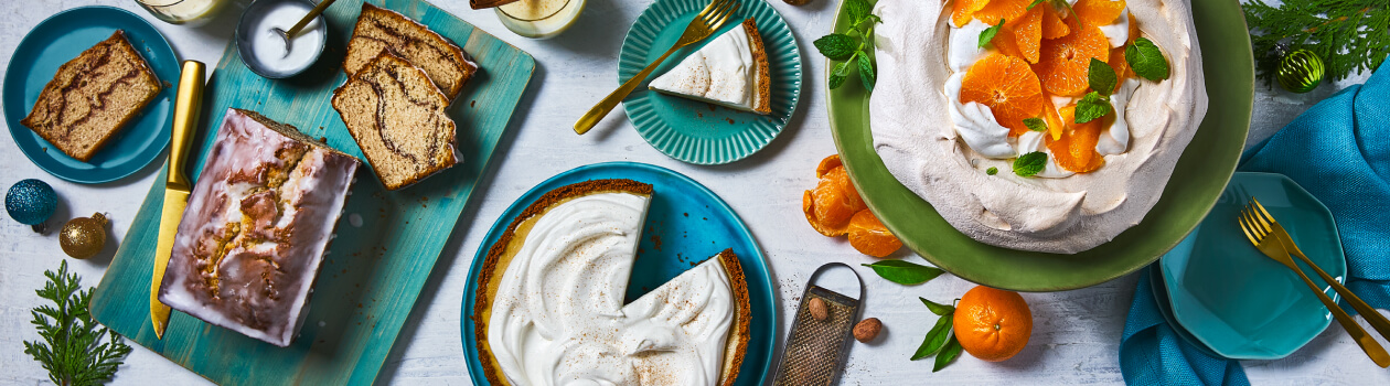 Overhead shot of eggnog desserts including loaf, cheesecake and pavlova.