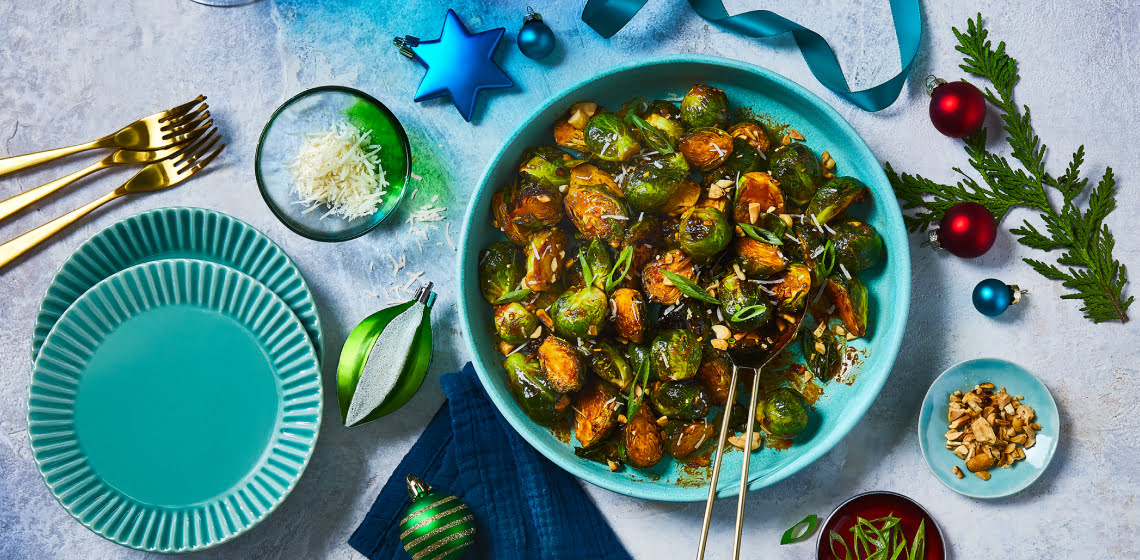 Bowl of gochujang brussel sprouts with peanuts and green onions to the side