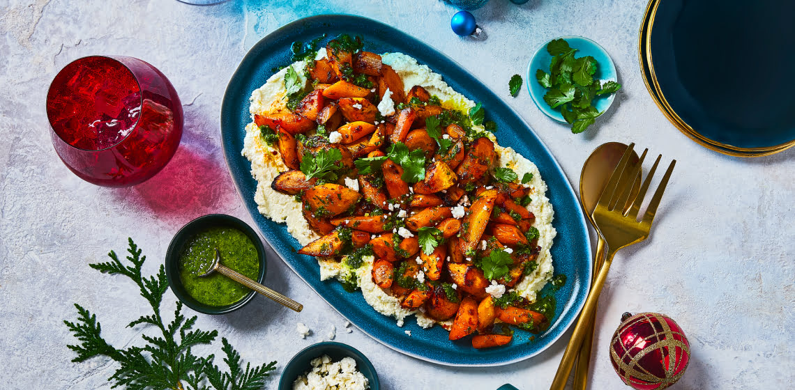 Harissa roasted carrots on a blue dish sitting on a bed of Zhoug