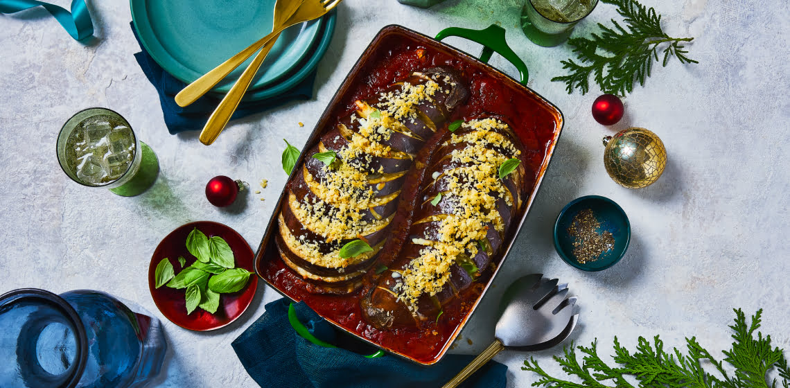 Two hasselback eggplants in a tray covered with cheese and sauce.