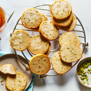 Rasmalai shortbread cookies on a cooling rack set on white countertop next to cup of tea and side plate of half-eaten cookies