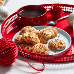 A white plate of roasted chestnut shortbread cookies, a glass of milk and a cup of tea on a red serving tray