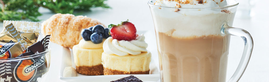 light blue table surface with a serving plate of glazed cinnamon buns, two whip cream topped lattes, and a casserole dish of strata