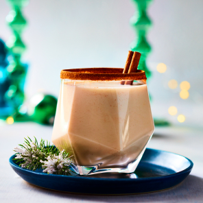 Whiskey snowball in an angular gem-cut drinking glass with a cinnamon stick garnish on a set holiday table