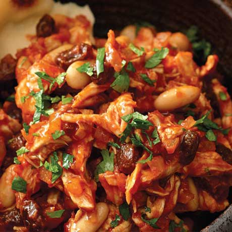 A black/brown bowl of bean turkey curry simmered in a tomato sauce.