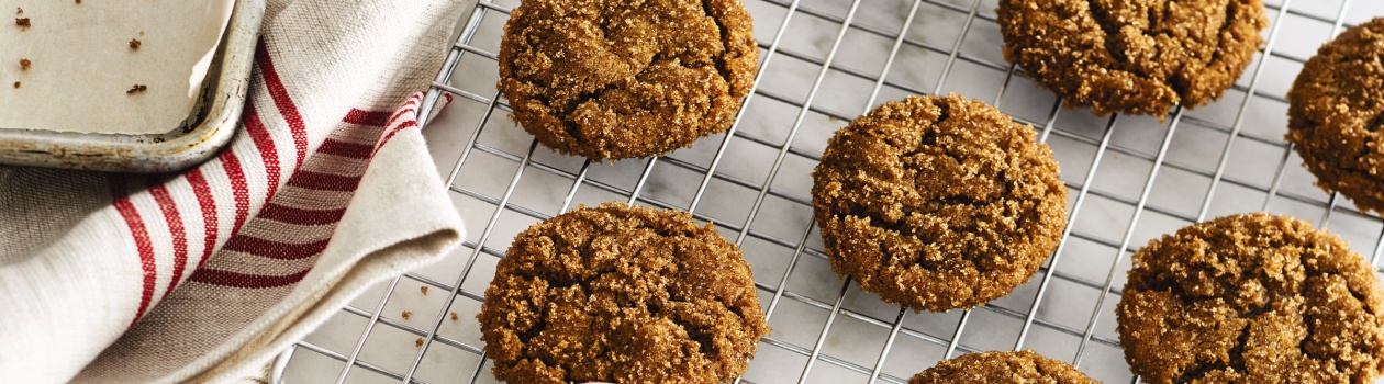 Chewy ginger molasses cookies on a cooling rack and in a white bowl on a white countertop