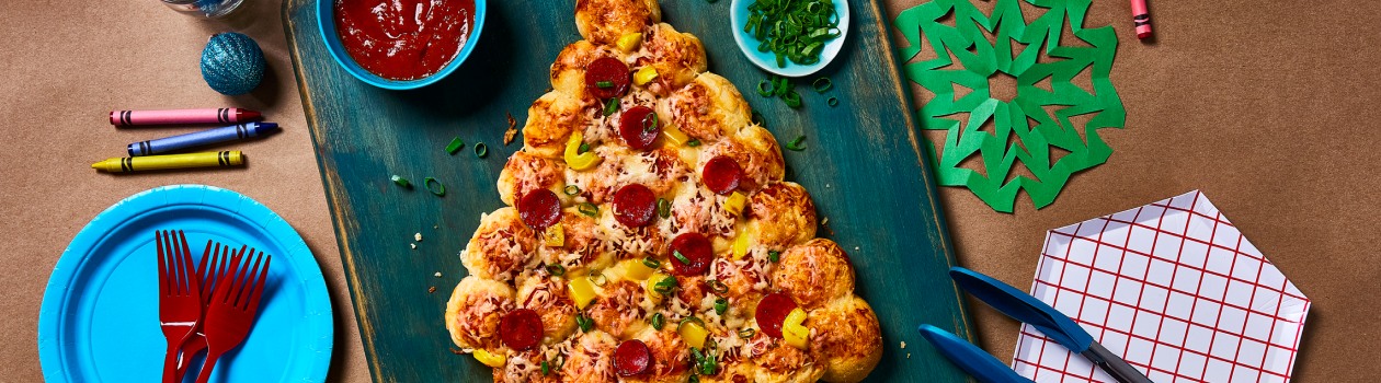 PIzza buns shaped into a Christmas tree topped with pepperoni and peppers on a blue cutting board.