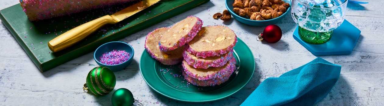 A log of icebox cookie dough on a board with a few cut off beside a teal plate stacked with more icebox cookies