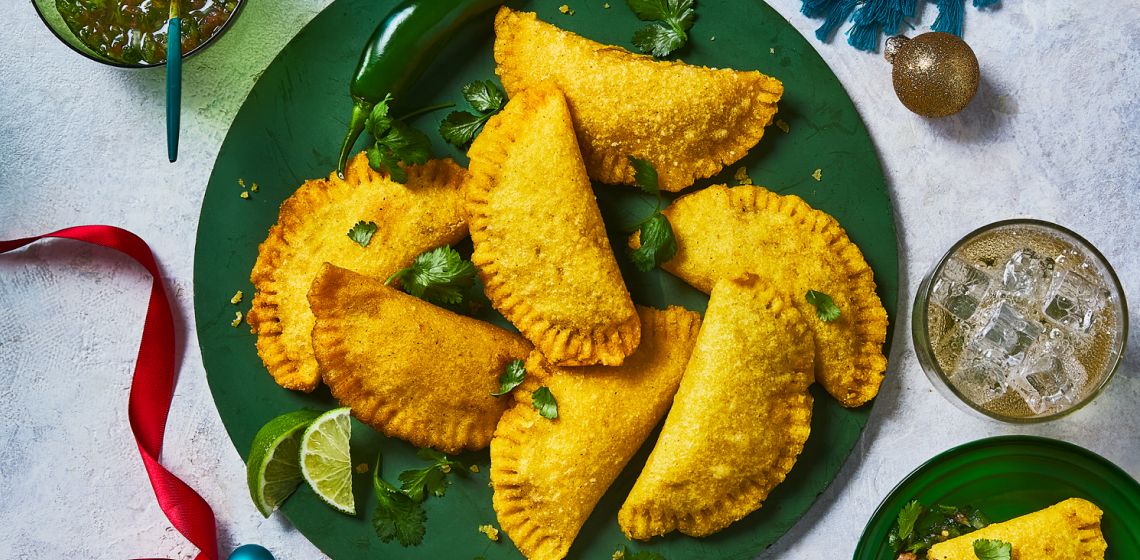 A green plate filled with empanadas, herbs and lime