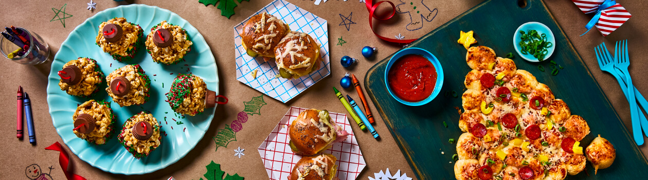 Overhead shot of pizza bites shaped like Christmas tree, ham and cheese sliders, and lasagna bites.