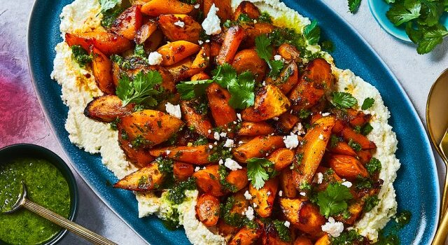 Harissa roasted carrots on a blue dish sitting on a bed of Zhoug