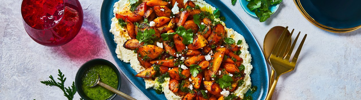 Harissa roasted carrots on a blue dish sitting on a bed of Zhoug