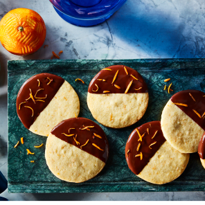 Several chocolate clementine icebox sugar cookies half dipped in chocolate with orange zest sitting on blue plates.