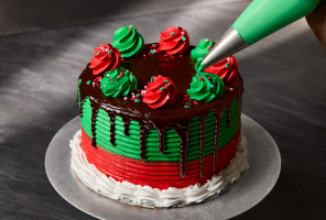 Green and Red Iced Cake with dripping chocolate ganache and red and green rosettes being added to the cake