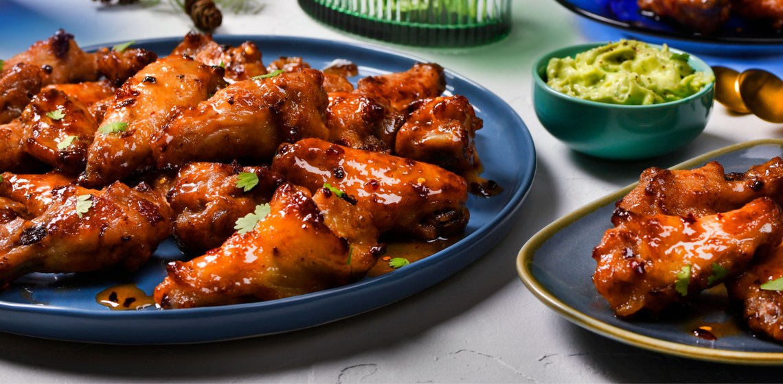 Hot honey wings on a blue plate and avocado, lime and cilantro dip in a bowl