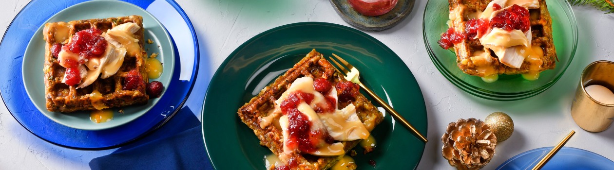 Three holiday dinner waffles, one on a green plate, one on a blue plate and one on a clear green plate