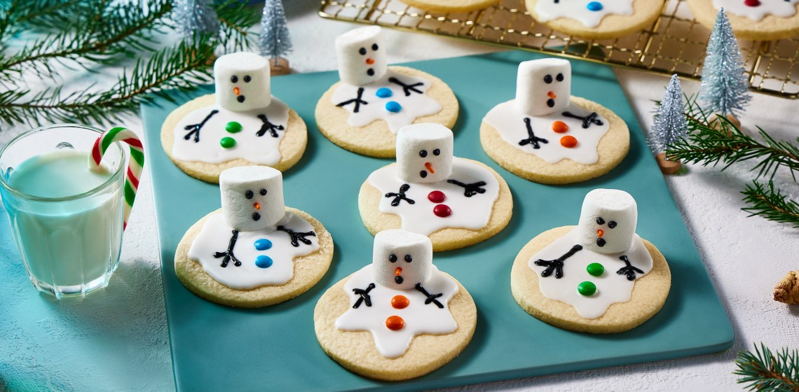 Melting snowman sugar cookies on a blue board with more in the background on a cooling rack