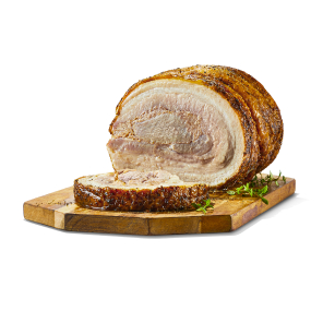 A pork porchetta roast with a slice cut, sitting on a wooden cutting board with some herbs