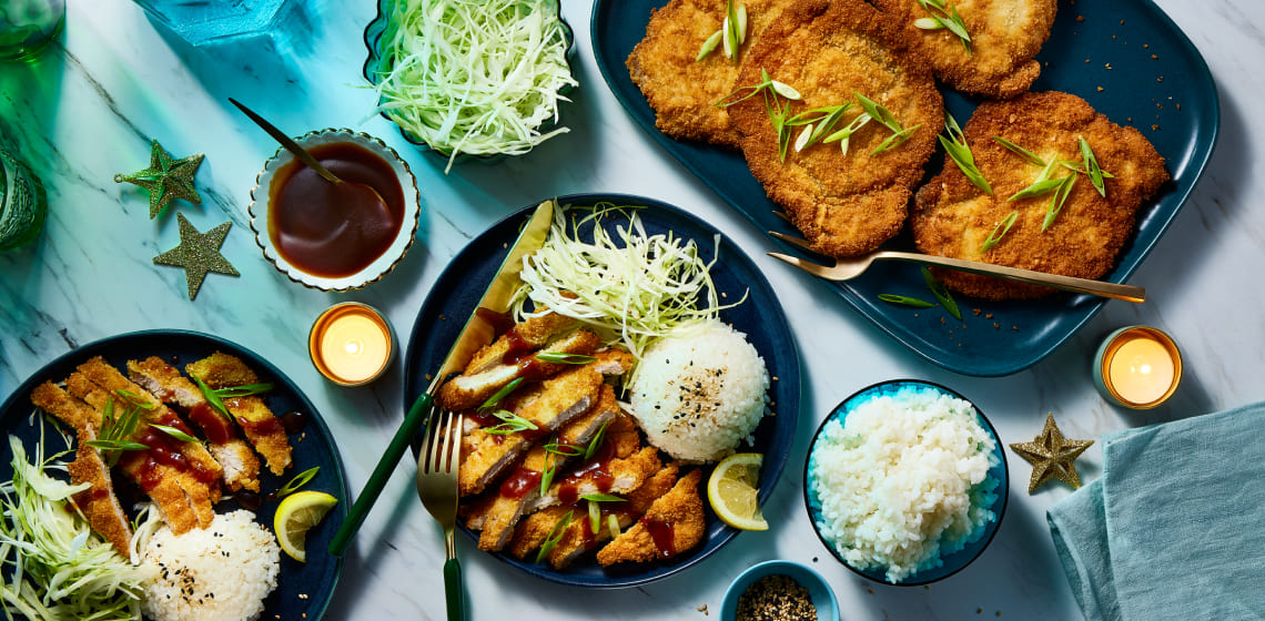 Sliced pork katsu on blue plate with a side of rice. Full pieces of katsu to the side on a blue serving platter