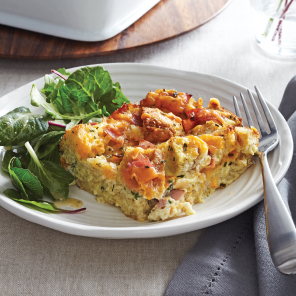 Slice of ham and cheese bread pudding on a plate with a side salad.