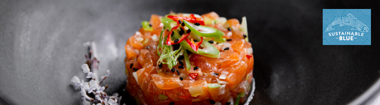 Salmon tartare in the centre of a black plate