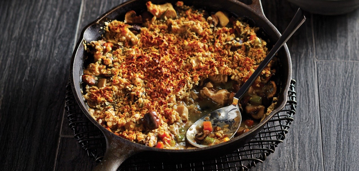 A skillet chicken pot pie with a portion scooped out on a dark wooden background