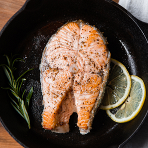 A cooked salmon steak in a skillet with slices of lemon and herbs