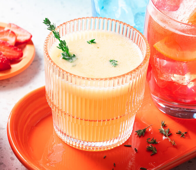 Tumbler glass filled with a slushy-type beverage made of citrus sorbet, citrus soda and tonic water on an orange platter.