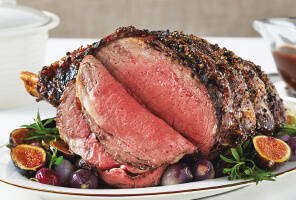 Sliced roast on white serving tray surrounded by figs, shallots, and rosemary