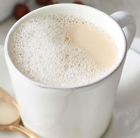 White mug with frothed green tea and hazelnut milk substitute.