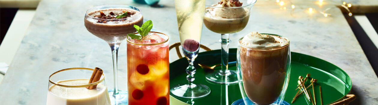 Group shot of holiday cocktails on a white marble surface, including a Mistletoe Martini, French 57, and a Ro-cocoa.