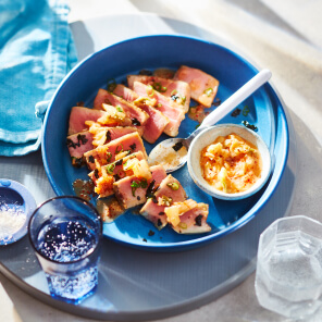 Sliced of seared tuna steak on a blue platter next to a bowl of miso kimchi butter.