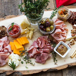 Charcuterie board with deli meats, cheese, olives, bread sticks, jams and grainy mustard.