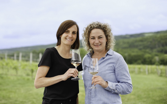 Two women standing in a field both holding a glass of white wine each.