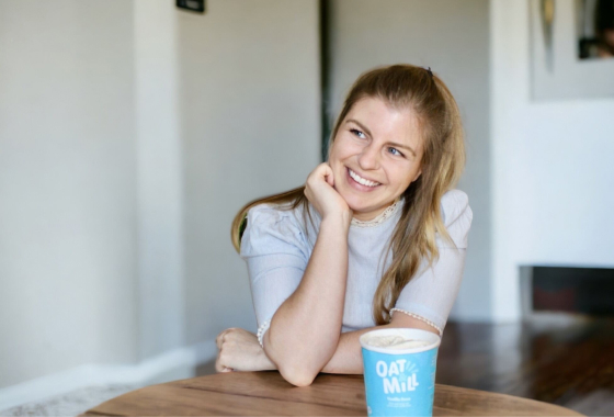 A woman leaning on a table with a pint of Oat & Mill ice cream in front of her.