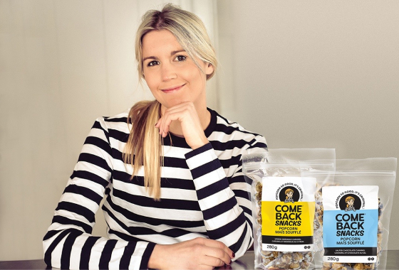 A blond woman in a black and white shirt with two bags of popcorn beside her.