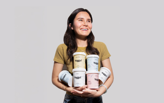 A brunette woman standing and holding six pints of Yoggu in her arms