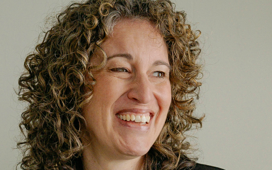 A woman in a green top and a black blazer with curly hair.