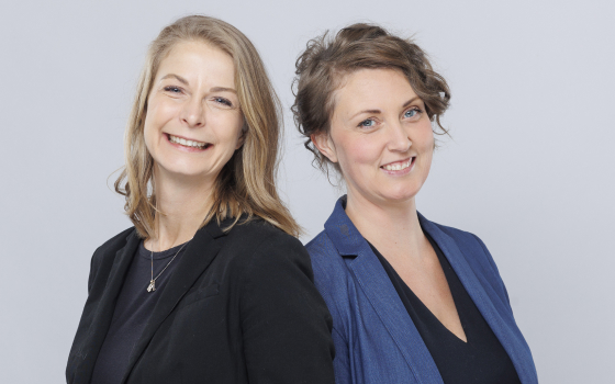 Two women standing back-to-back, one in a black blazer and another in a blue blazer